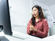© kan - Confident Asian female call center agent with headset talking to client support for customer care in office. Asian woman telemarketing agent working on computer for consulting, customer support.