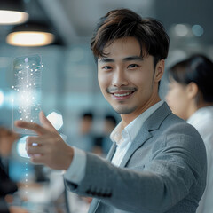 Aufkleber - young Asian man, dressed in smart grey business attire, reaching out to a white background to touch a digital image floating in his hand. In the background are scenes of other staff members working.