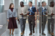 © Seventyfour - Full length shot of positive African American male boss dressed in smart casual clothes talking to smiling employees while walking along business center hallway