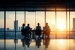 Four business professionals, silhouetted by the setting sun, engage in discussion around a large conference table in a high-rise building, symbolizing collaboration.