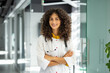 © Liubomir - Smiling female doctor with curly hair and stethoscope standing confidently in medical office. Represents healthcare professionalism, trust, and positive environment.