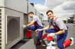 © Studio Romantic - Portrait of a smiling electrician using tools and equipment, installing, maintaining, or repairing an HVAC system on the roof. Couple of workers ensures proper air ventilation system functionality.