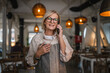 © Miljan Živković - mature woman waitress stand at restaurant and talk on mobile phone