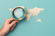 © Mongkol - Exploring Global Investments, a hand examines a world map with a magnifying glass, seeking undiscovered financial prospects.
