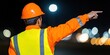 © Kamonwan - Construction worker directing traffic in bright orange safety gear at night.