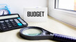 © Sviatlana - The concept of budget planning. Notepad with the word 'Budget', calculator, clock, magnifying glass on a white background.