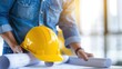 © Vilaysack - Construction worker examining blueprints with a yellow safety helmet on a desk in a bright office environment