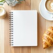 © WE.ARE.AI - Blank sketchbook on a polished wooden counter, with freshly brewed coffee and a croissant, morning creative ritual