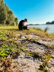 Wall Mural - a man is sitting on the grass by a body of water