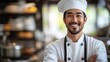 © YURY YUTY - A smiling chef in a professional kitchen wearing a chef's hat and coat.