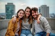© Viktor - Three young adults sit outdoors on city rooftop terrace. Smiling, embracing. Casual clothes. Evening light. Urban cityscape background. Friends bond togetherness. Lifestyle photo. Enjoying time