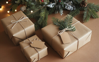 Gift boxes wrapped in craft paper beneath spruce branches, creating a festive Christmas scene on a brown wooden background, ideal for holiday designs.

