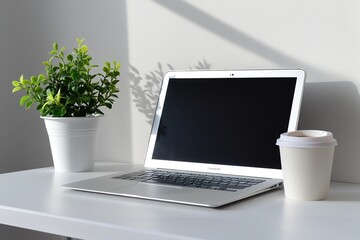 Wall Mural - Modern laptop on a white desk with a potted green plant and a takeaway coffee cup in soft natural light