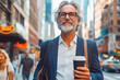 © VisualProduction - Happy businessman holding coffee and smartphone walking in the city