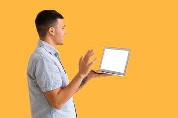 Wall Mural - Young man with blank laptop video chatting on yellow background. Online dating concept