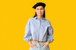 © Pixel-Shot - Beautiful young woman in stylish black beret hat on yellow background