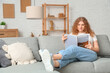 © Pixel-Shot - Young woman reading magazine on sofa at home