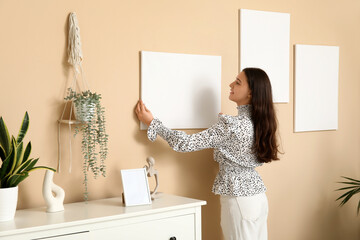 Young woman hanging empty canvas on beige wall at home