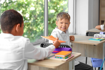 Wall Mural - Little schoolboy handing copybook to her classmate in classroom