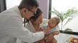 © Krakenimages.com - Doctor examines baby boy held by mother in clinic room, showcasing a warm family moment indoors with a pediatrician attending to the patient in a professional setting.