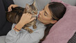 © Krakenimages.com - A young hispanic woman lounges in her living room, affectionately holding her cat indoors.