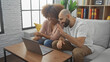 © Krakenimages.com - An interracial couple is laughing together while looking at a laptop in a modern living room.