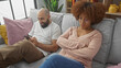 © Krakenimages.com - An interracial couple is relaxing on a couch at home, the man smiling with his smartphone while the woman appears upset.