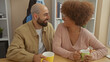 © Krakenimages.com - A cheerful interracial couple enjoys a cozy coffee break together indoors, sharing a laugh in a casual home setting.