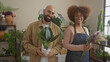 © Krakenimages.com - A smiling man and woman, holding plants, stand side by side in a flower shop filled with various flora.