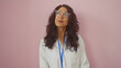 © Krakenimages.com - Middle-aged hispanic woman in a lab coat with glasses smiling over a pink background.