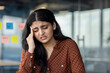 © Liubomir - Latin American businesswoman with headache feeling stress while in office. She shows discomfort and contemplation, symbolizing work stress and health concerns.