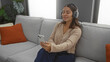 © Krakenimages.com - Woman relaxing on a sofa indoors with headphones and smartphone, enjoying music in a cozy living room setting, showcasing a calm and serene atmosphere.