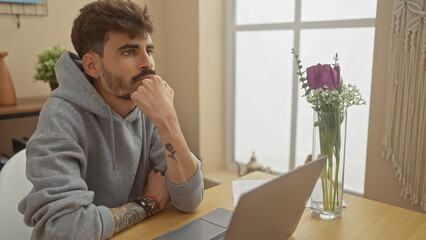 Wall Mural - Pensive young man studying with laptop in cozy living room.