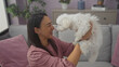 © Krakenimages.com - A happy woman indoors lovingly holds a fluffy white bichon maltese dog in a modern living room.