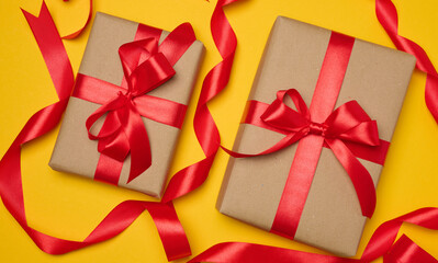 Wall Mural - Two boxes tied with red ribbon on yellow background, festive background.