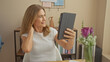 © Krakenimages.com - Mature woman using tablet at home with bookshelf and flowers in background.