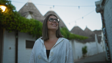 Wall Mural - A young hispanic woman smiling and exploring the charming old town streets of alberobello, italy, known for its iconic trulli houses, in the beautiful region of puglia.