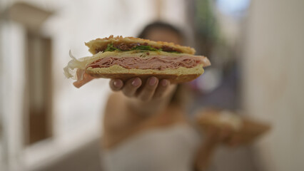 Wall Mural - Young hispanic woman enjoying a puccia sandwich on the streets of gallipoli, puglia, italy, showcasing a delicious ham-filled bread in a vibrant european setting.