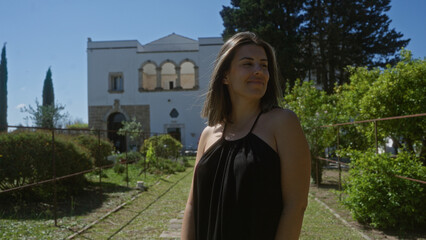 Wall Mural - A young, beautiful hispanic woman standing outdoors at a villa in puglia, italy, surrounded by lush greenery and historical architecture.