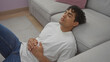 © Krakenimages.com - A young hispanic man in casual attire relaxes on a sofa in a modern living room, embodying tranquility and domestic comfort.