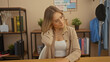 © Krakenimages.com - A beautiful young blonde woman is sitting in a cozy home office, thoughtfully touching her neck, surrounded by shelves with books and plants.