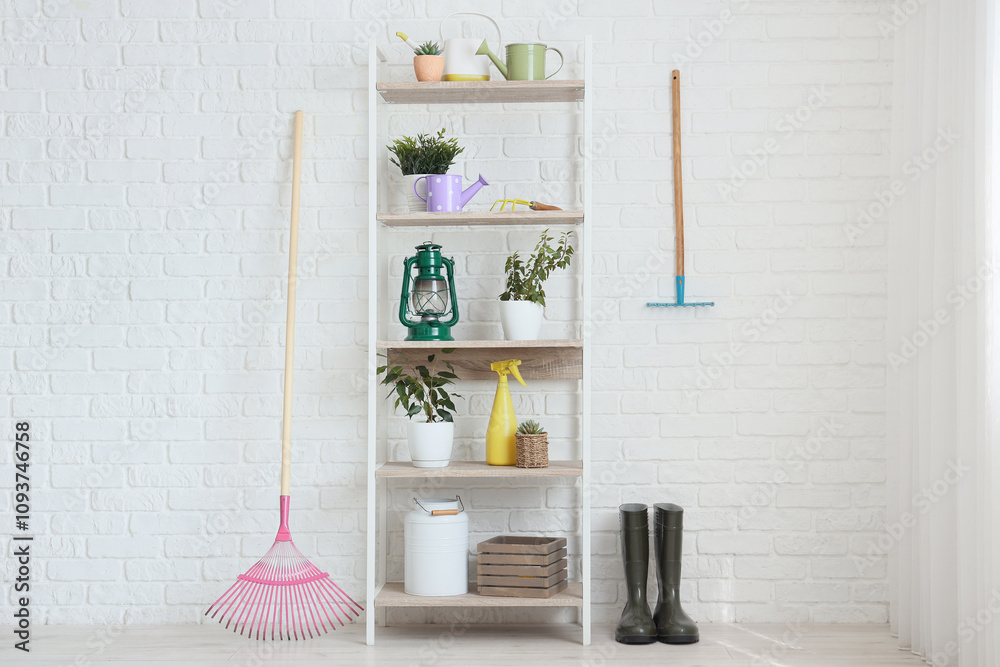 Shelf unit with plants and gardening tools near white brick wall in workshop