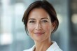 © Nognapas - Close-up headshot of confident European mature, good looking middle-aged leader, businesswoman CEO on blurred office background. Beautiful senior European businessman smiling at the camera