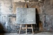 © juliars - Grey painted canvas on a wooden easel standing in front of a grungy damaged wall, creating a scene of artistic potential and urban decay