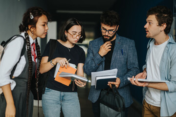 Poster - A group of diverse students consults with a professor in a hallway. They are engaged in a thoughtful academic discussion, showing collaboration and learning. Educational materials and notebooks are