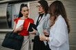 © qunica.com - Group of businesswomen having an outdoor meeting, discussing documents, and holding notebooks. Professional women collaborating on work tasks.