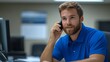 © 楠 刘 - IT professional in a blue polo shirt talking to a client on a cell phone while sitting in a modern office, showcasing communication, technology, and professionalism in a work setting.