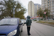 © Mihail - A woman dressed in warm clothing opens the door of a car parked on a city street surrounded by modern buildings.