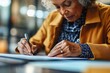 © Margarita - Elderly Woman Writing at Desk in Modern Office Setting