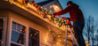 © Taiwo - Man on a ladder decorating house with LED outdoor fairy lights for Christmas celebration season greetings. Outdoor holiday Christmas light installation.